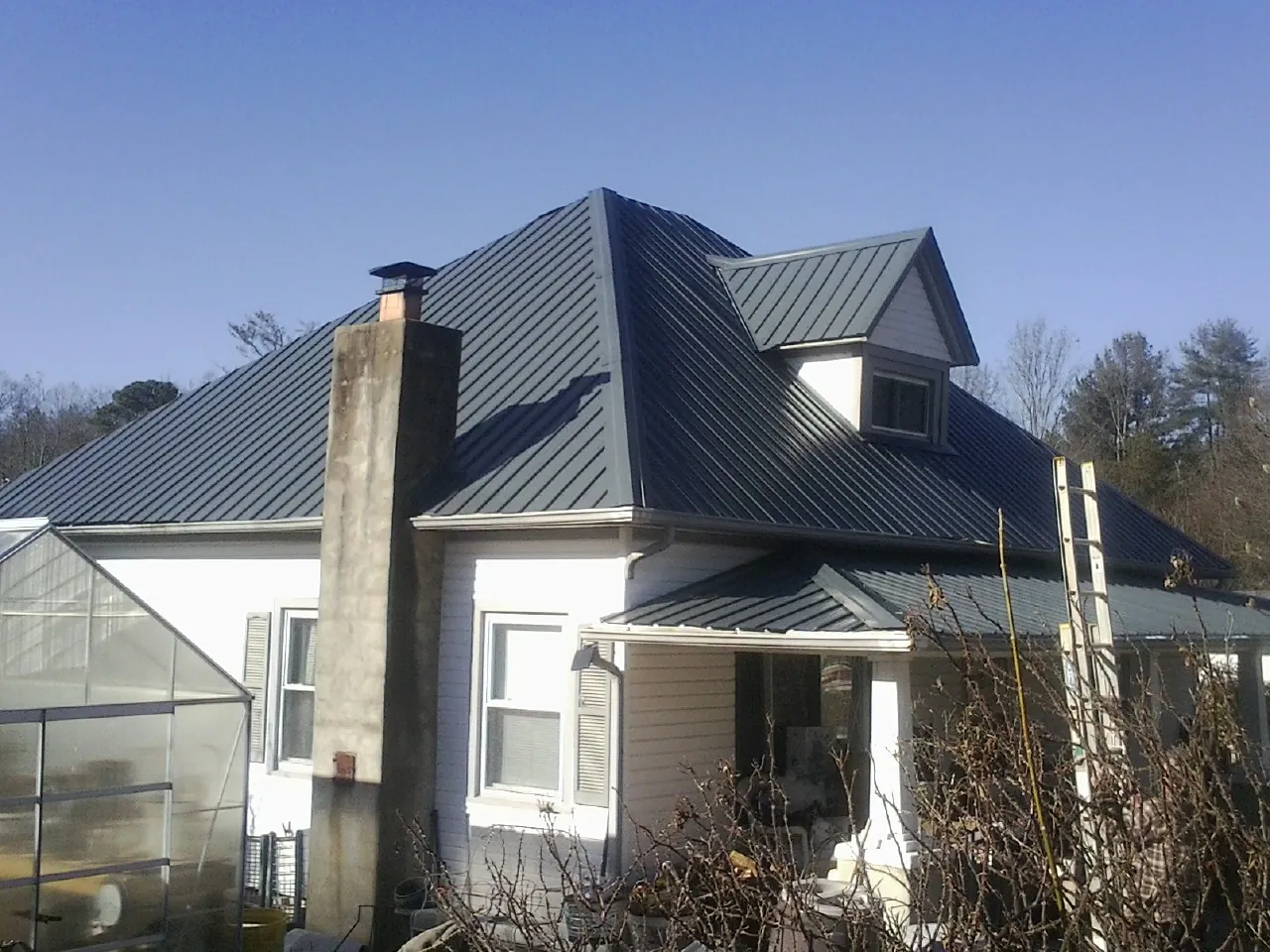 Dark blue standing seam metal roof on a white farmhouse with dormer in Sand Lake