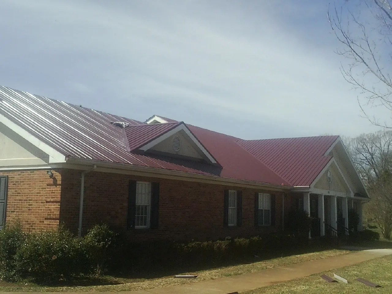 Red metal roof with gabled entries on a long brick building, from a Hail Damage Roof Repair job in Sand Lake