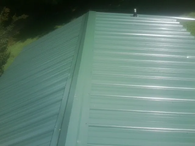 New green metal panels meeting at the ridge of a roof — Flat Roof Repair work by our crew in Sand Lake