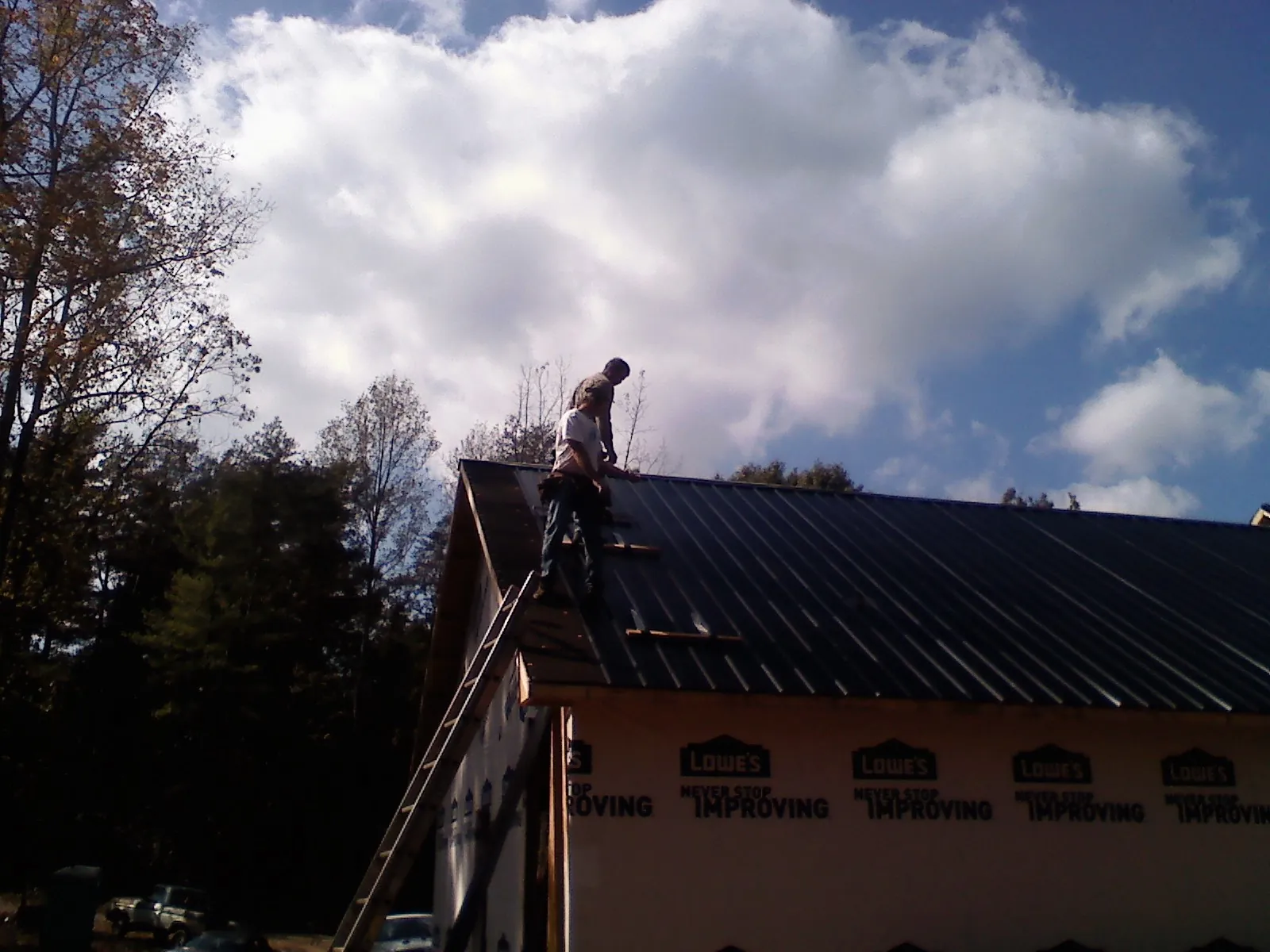 Roofer fastening dark metal panels high against a cloudy sky, from a Roof Inspection job in Sand Lake