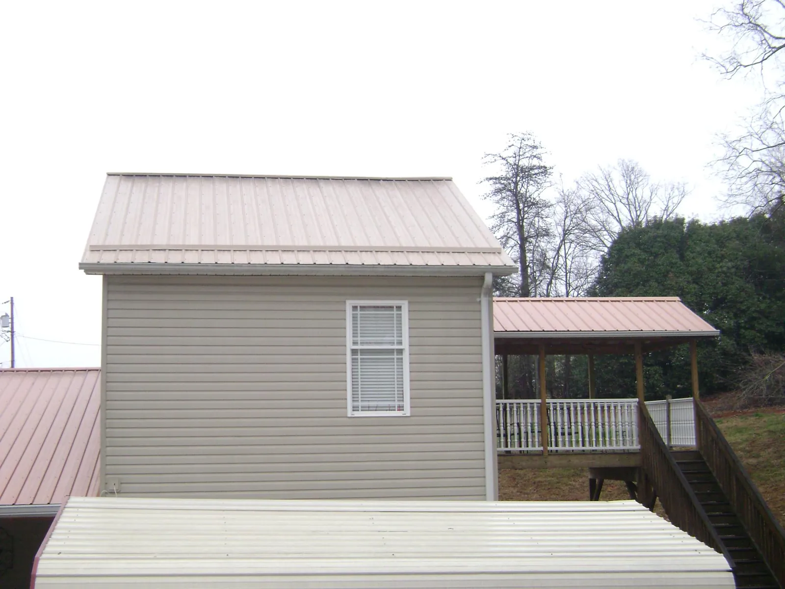 Tan metal roofs on a two story addition and attached porch, from a Roof Replacement job in Sand Lake